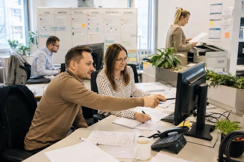 Zespół w biurze, dwie osoby analizują zestawienie na monitorze