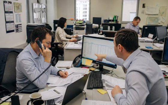 Dwoje pracowników przy biurku w open space, rozmowa telefoniczna i praca na dwóch monitorach